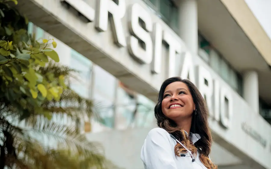 A smiling doctor in a white coat outside a university building
